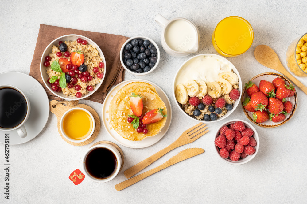 A table for a healthy breakfast of pancakes, granola, fresh berries, coffee with milk and orange juice. Top view. A table for a healthy breakfast of pancakes, granola, fresh berries, coffee with milk and orange juice. Top view.