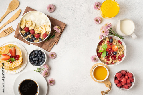 A table for a healthy breakfast of pancakes, granola, fresh berries, coffee with milk and orange juice. Top view.