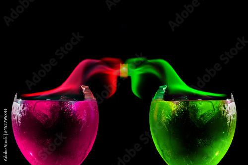 Taças de vidro quebras contendo liquido de cor verde e cor de rosa com chamas das mesmas core se tocando no alto.  photo