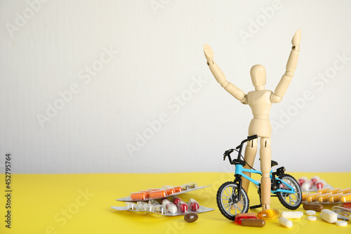 Pills, sportsman and bike model on yellow table, space for text. Using doping in cycling sport concept