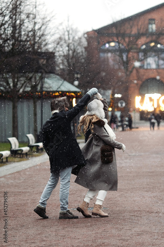 Joyful young couple travel on Christmas enjoy walking outdoors spinning and dancing in empty old town. Happy lovers have fun outside on street in snow dressed in warm clothes during vacation together