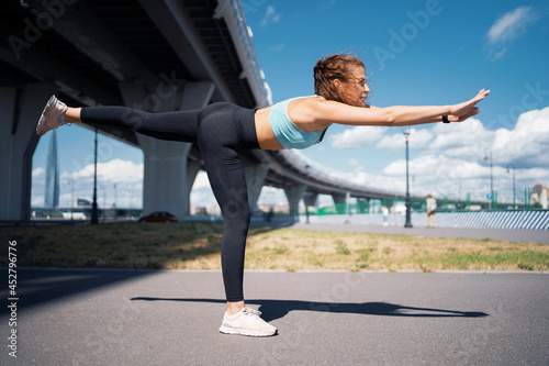 A strong athletic woman does exercises outdoors. The trainer is engaged in fitness on the street. Healthy lifestyle, sports activities in the city. A smart watch on your hand.