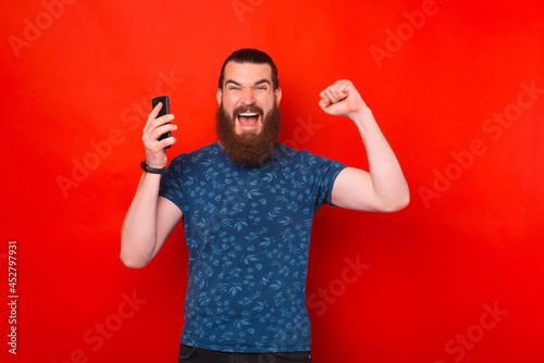 A winner bearded man is holding his phone and screaming at the camera.