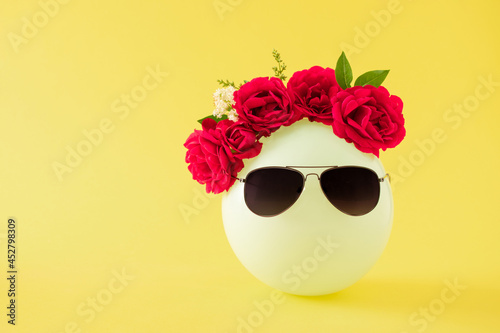 Fototapeta Naklejka Na Ścianę i Meble -  Creative arrangement of balloon with decoration of red roses and leaves and black sunglasses against bright yellow background. Minimal end of summer concept. Copy space.