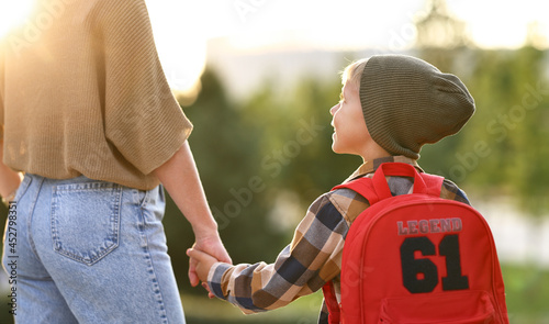 Loving mother and little son schoolboy with backpak holding hands while going to school together photo