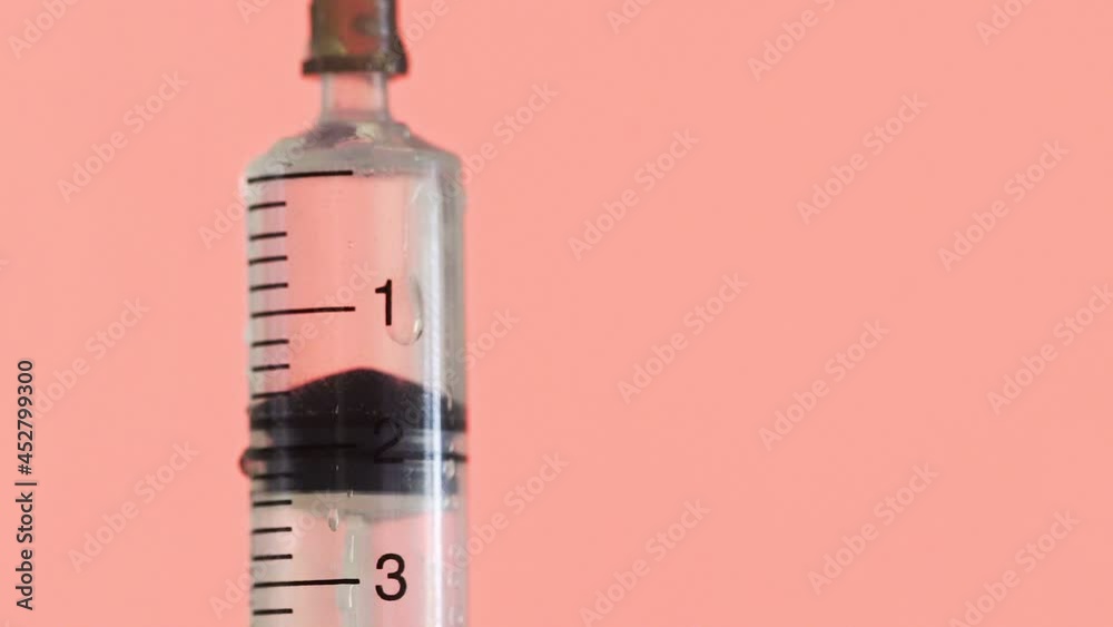 Close-up of a needle from a disposable syringe. A small syringe pushes the liquid out of the hole on a red background Close-up of a needle from a disposable syringe. A small syringe pushes the liquid out of the hole on a red background
