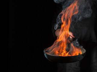 Professional chef cooking food in pan with fire flame on black background. Restaurant and hotel service concept. Free advertising space