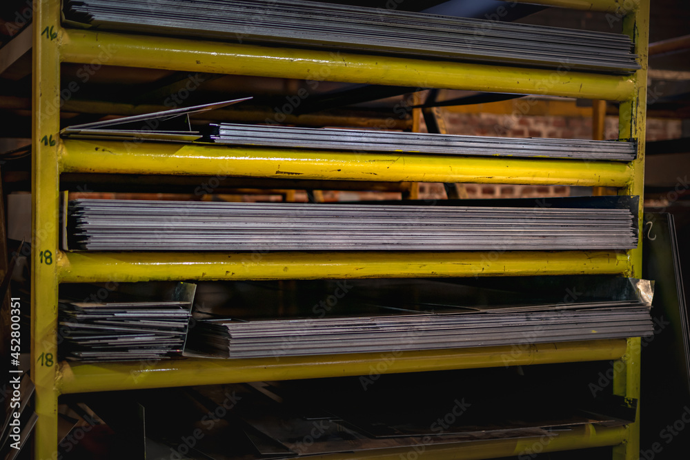 Piles of metal sheets stored in yellow shelves on a factory