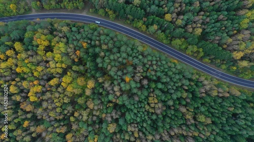 Arial view of car on a narrow twisting road. Autumn colorful trees by the sides of the road