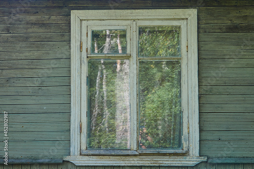 Old white wooden window in an old wooden rustic green house with green plank walls 
