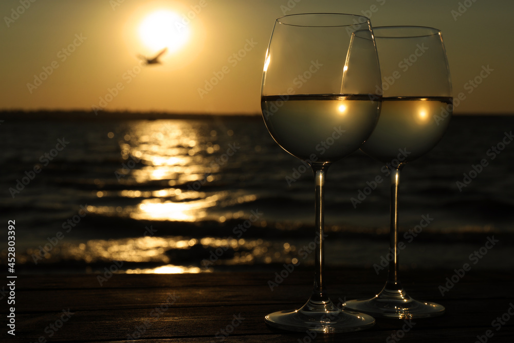 Glasses of delicious wine near sea at sunset