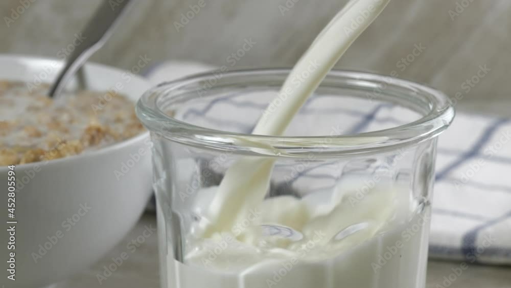 Pouring milk into a glass next to a bowl of almond granola
