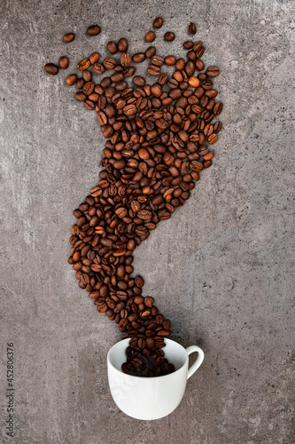 Spilled cup of coffee with beans as smoke shape photo