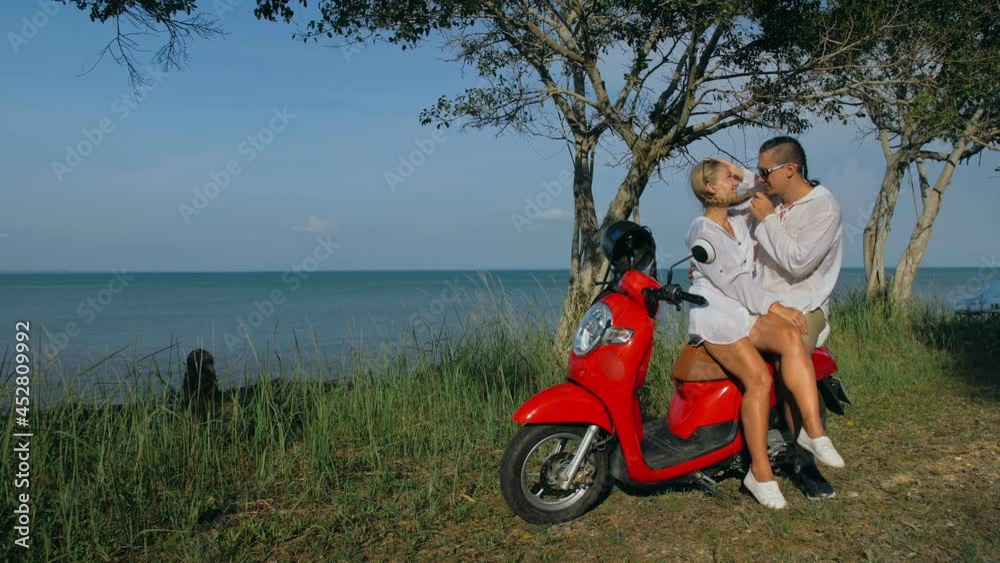 Love couple on red motorbike in white clothes on forest road trail trip. Two caucasian tourist woman and man kiss hugs sit on scooter. Motorcycle rent Safety helmet sunglasses. Asia Thailand tourism. Love couple on red motorbike in white clothes on forest road trail trip. Two caucasian tourist woman and man kiss hugs sit on scooter. Motorcycle rent Safety helmet sunglasses. Asia Thailand tourism.