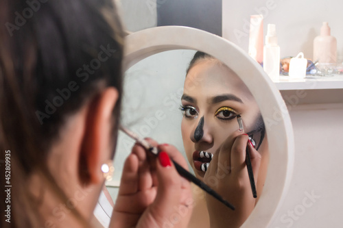 Fotografie Beautiful girl doing her skull teeth makeup for Halloween with her little mirror in her room
