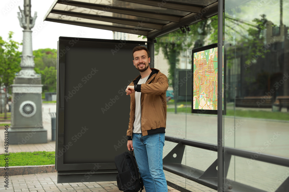 Young man with backpack waiting for public transport at bus stop Young man with backpack waiting for public transport at bus stop