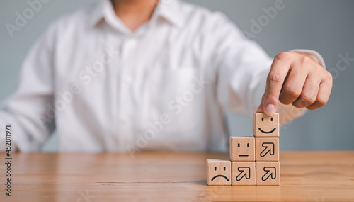 Hand of a businessman chooses a smiley face on wood block cube, The best excellent business services rating customer experience, Satisfaction survey concept.