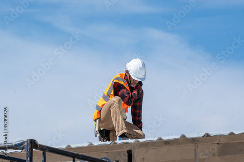 Roofer worker in protective uniform wear and gloves working installing metal sheet on top of the new roof at construction site.