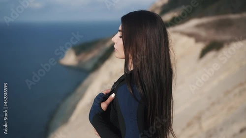 Slow motion side view of sexy young athletic woman taking off her jacket on the seashore enjoying the fresh breeze and the view of the waves. Training preparation concept