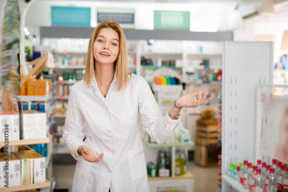 Ordinary glad cheerful positive woman pharmacist showing assortment of drugs in pharmacy