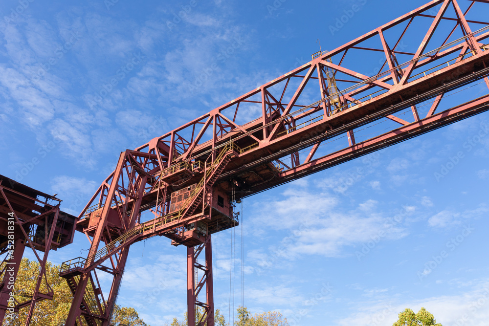 Huge overhead trolley structure, rusted metal industrial architecture against a blue sky, horizontal aspect