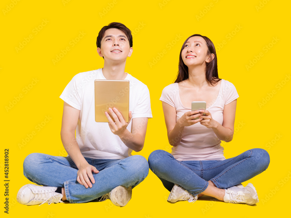 Young man and woman using tablet computer and smartphone.Isolated on yellow background.Look above.