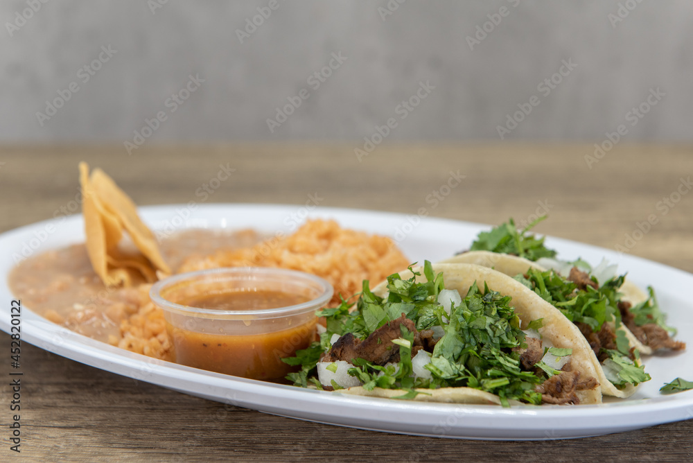 Hearty plate of three loaded carne asada tacos with cilantro, served with rice and refried beans