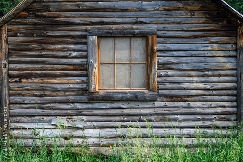 Bild auf Leinwand Rustic log cabin with wood frame window and tall grass in front, on a sunny day
