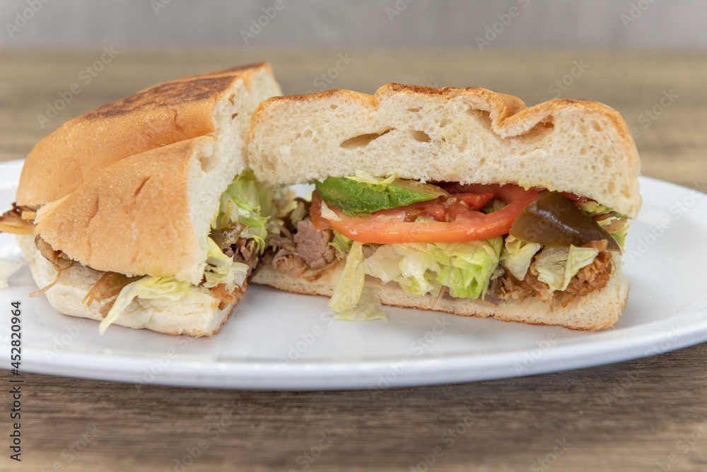 Hearty carnitas pork torta sandwich cut in half to show all the chopped peppers and vegetables with the meat and bread bun Hearty carnitas pork torta sandwich cut in half to show all the chopped peppers and vegetables with the meat and bread bun