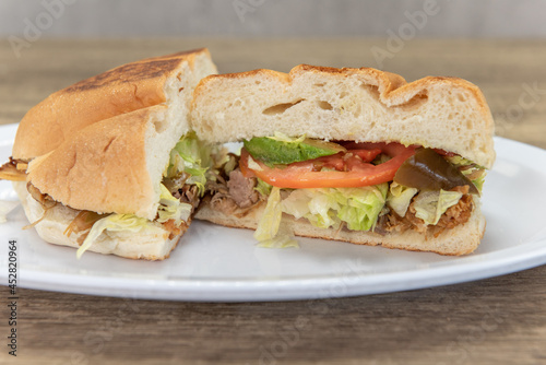 Hearty carnitas pork torta sandwich cut in half to show all the chopped peppers and vegetables with the meat and bread bun