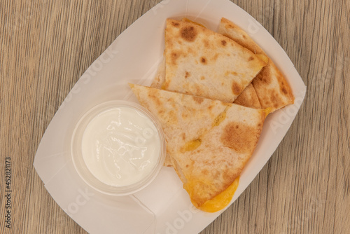 Overhead view of hearty appetizer of quesadilla wedges with melted cheese and sour cream as a dipping sauce