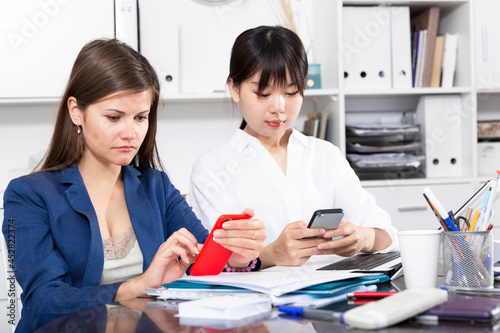 Two women write sms by phone in the office