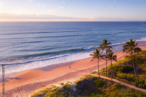 Aerial view over Gold Coast beach and ocean with palm trees and sunrise light.