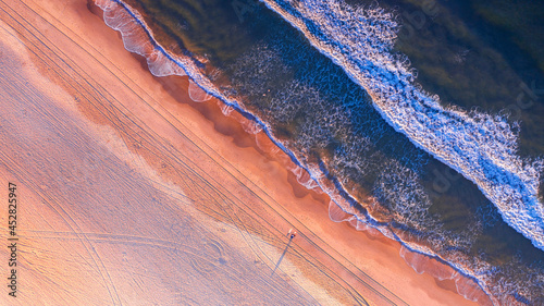 Aerial view over beach and ocean with sunrise light.
