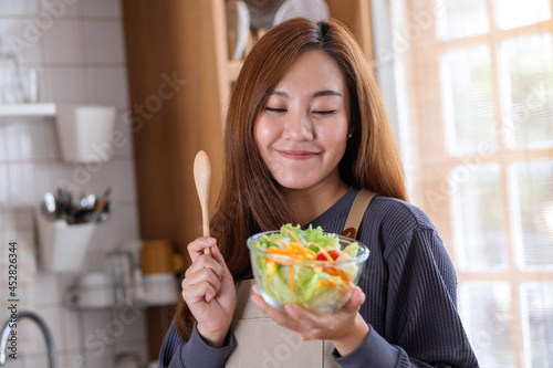 A young woman cooking and eating fresh mixed vegetables salad in the kitchen at home