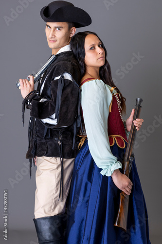 A pirate couple holding guns against a grey studio backdrop