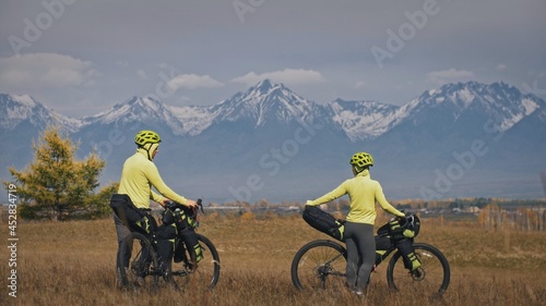 The man and woman travel on mixed terrain cycle touring with bikepacking. The love couple journey with tent in nature with bicycle bags. Stylish bikepacking, bike, sportswear in green black colors. photo