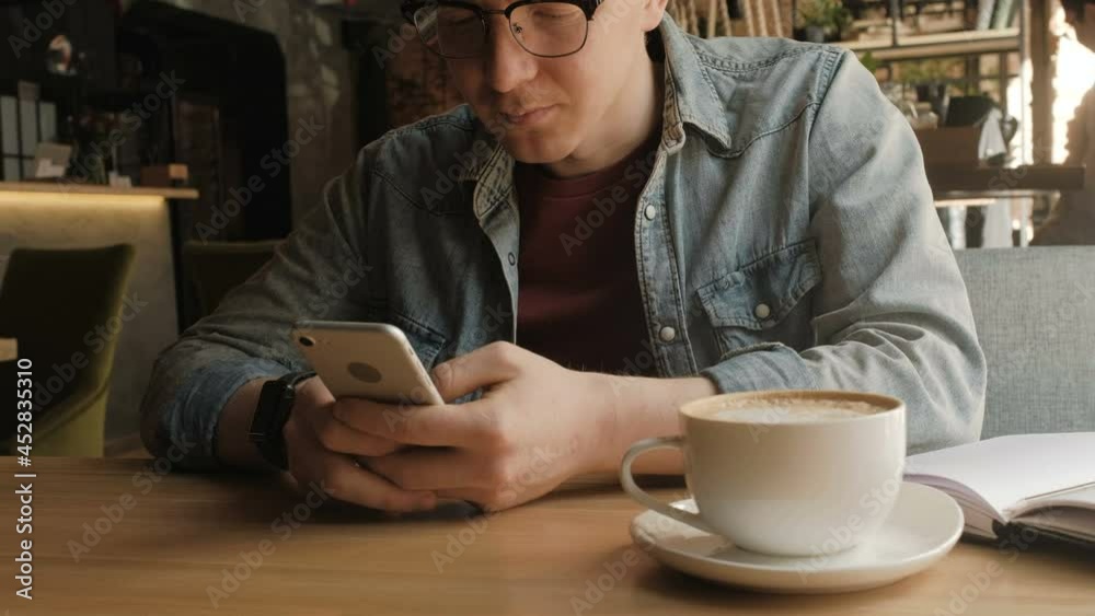Close up of man's hand holding smart phone and typing with a thumb. He is at the cafe. Still shot, low angle, anonimous Close up of man's hand holding smart phone and typing with a thumb. He is at the cafe. Still shot, low angle, anonimous