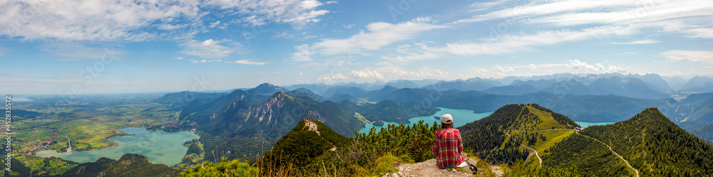 Woman sitting and relaxing at top of Mountain Herzogstand after hiking. looking at the spectacular bavarian Prealps mountains panorama with Lakes (Kochelsee, Walchensee) Europe, Germany