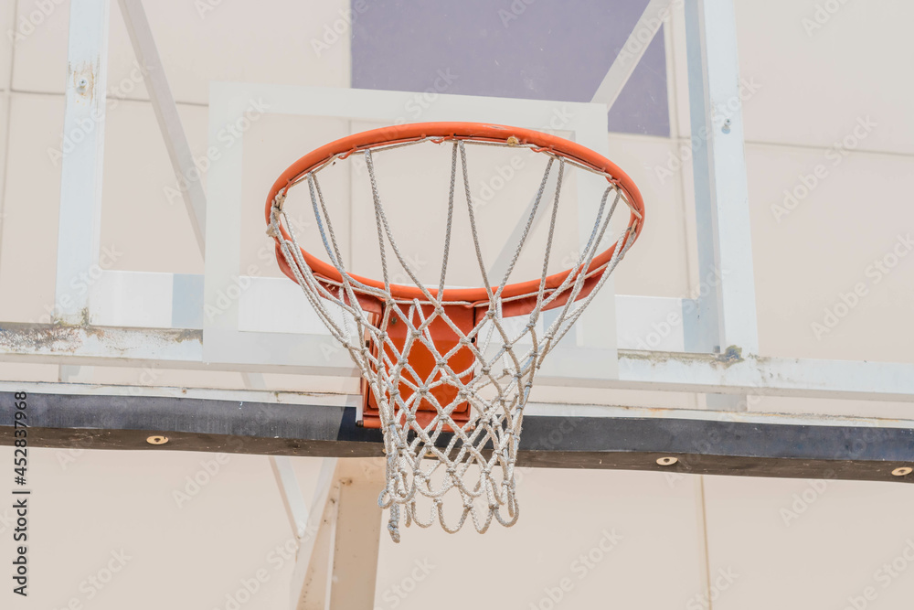 Closeup of orange basketball hoop with rope net against glass backboard.