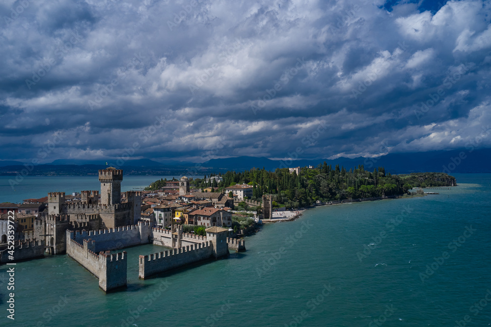 Rocca Scaligera Castle in Sirmione. Cumulus clouds over the island of Sirmione. Aerial photography with drone. Aerial view on Sirmione sul Garda. Italy, Lombardy