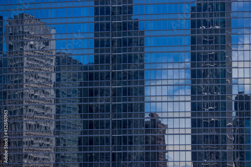 高層ビルのガラス窓に反射する隣のビルと雲