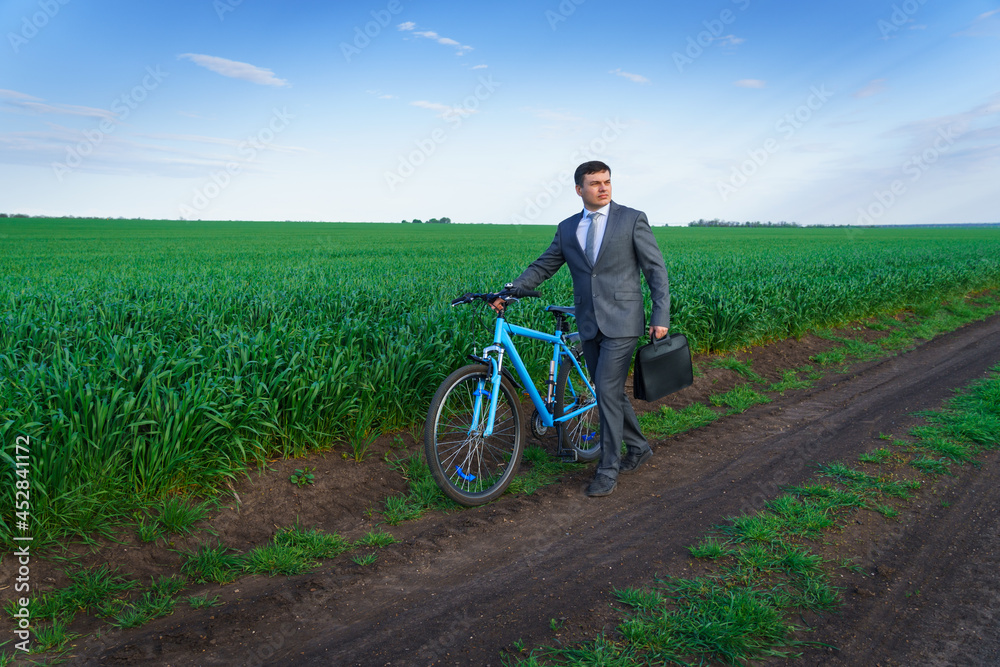 Obraz premium Businessman with a bicycle posing in a green grass field - business concept for freedom, vacation or freelance. Beautiful spring nature.