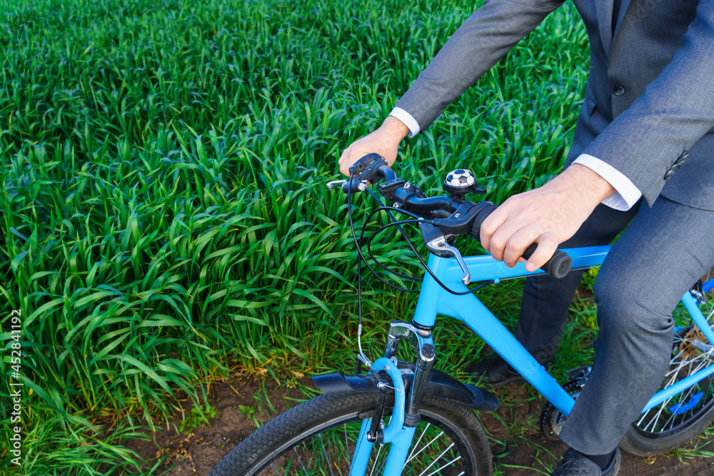 Obraz premium Businessman's hand with a bicycle posing in a green grass field - business concept for freedom, vacation or freelance. Beautiful spring nature.