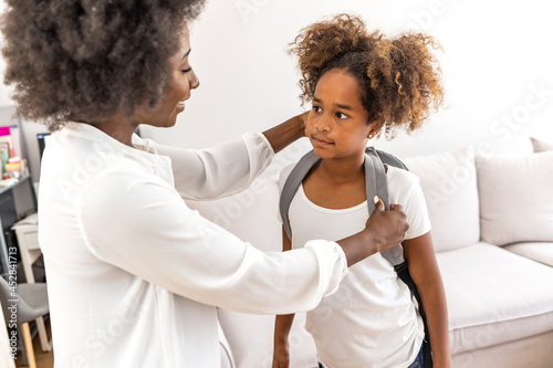 Mother taking daughter to school. Black woman in front hallway fixing young girls dress. Mother and daughter preparing the first day going study back to school. Student concept