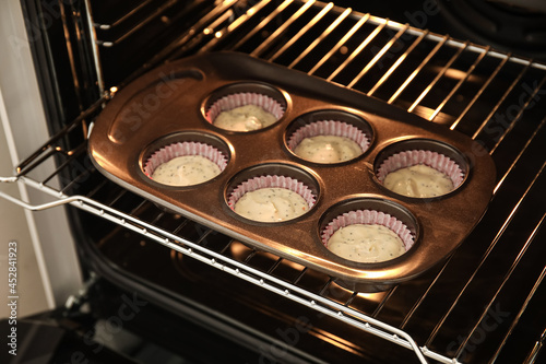 Baking tin with uncooked poppy seed muffins in oven