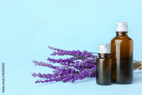 Bottles of lavender essential oil and flowers on color background