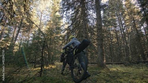 The woman travel on mixed terrain cycle touring with bike bikepacking outdoor. The traveler journey with bicycle bags. Stylish bikepacking, bike, sportswear in green black colors. Magic forest park.