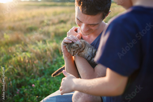 Young guy found and picked up little stripped kitten during walking in the field and going to home it, homeless domestic animals care, concept of volunteering and animal rescue