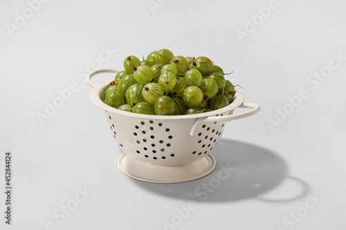 Colander with fresh ripe gooseberry on light background